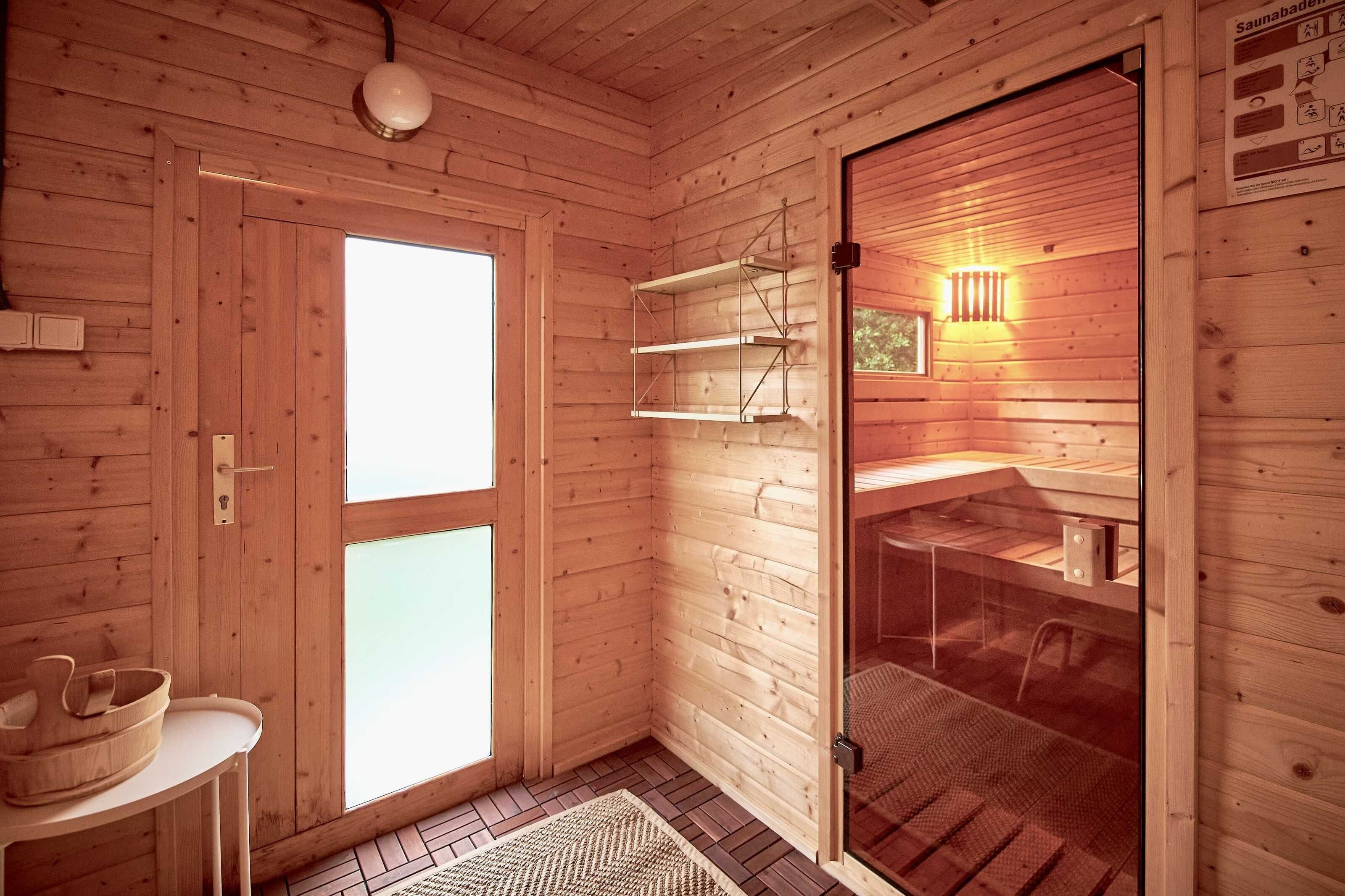 A wooden cabin interior with a glass door, a white table with a bowl, and a shelf with a hanging light.