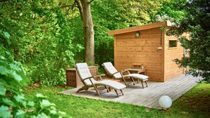 Une cabane en bois dotée d’une terrasse, de deux chaises longues et d’une petite table.