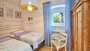 Une chambre d’hôtel avec deux lits, un fauteuil, une armoire en bois, une fenêtre avec des rideaux et des œuvres d’art mural.