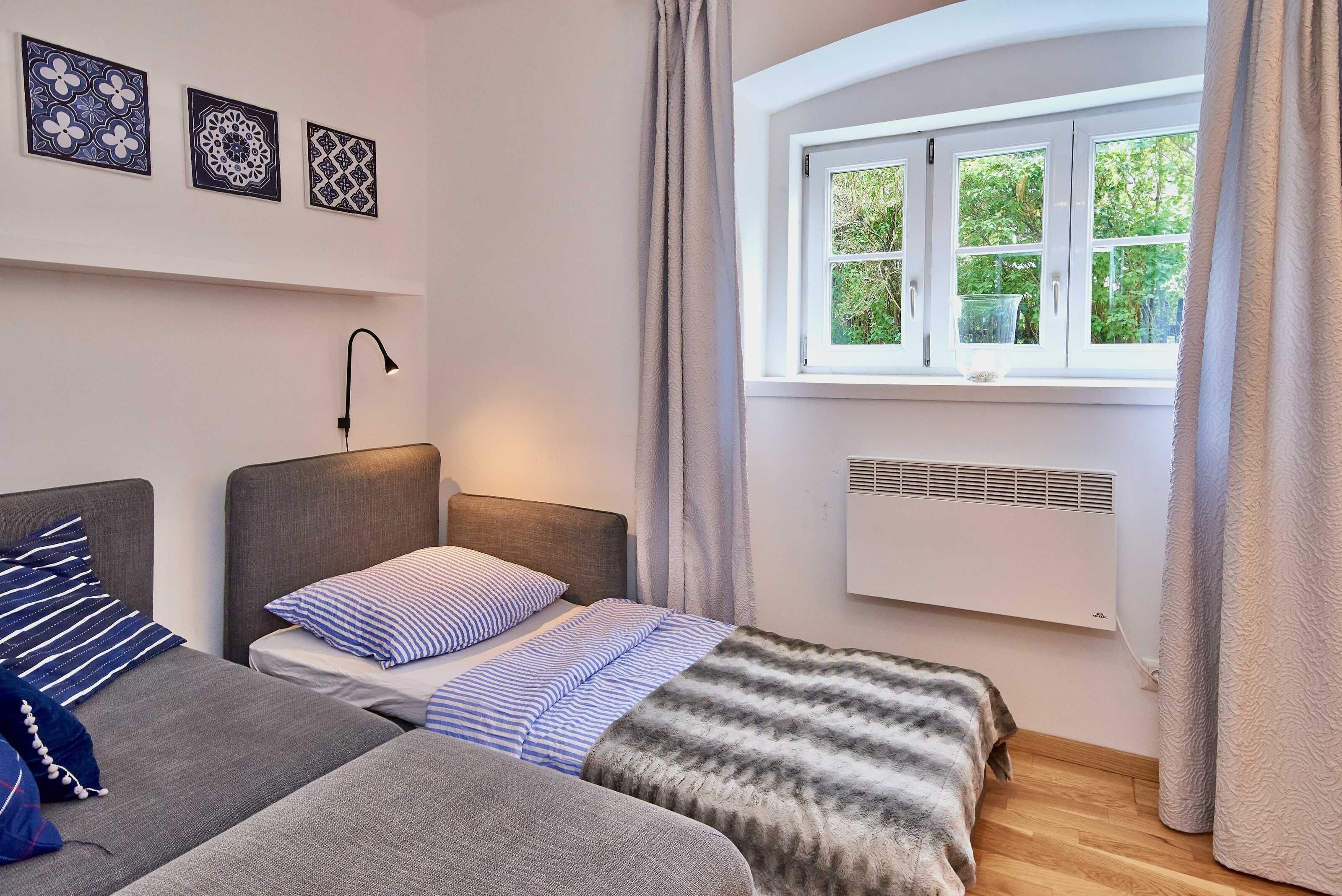 Een slaapkamer met twee bedden, een raam met gordijnen, een wandairconditioner en drie decoratieve muurpanelen.