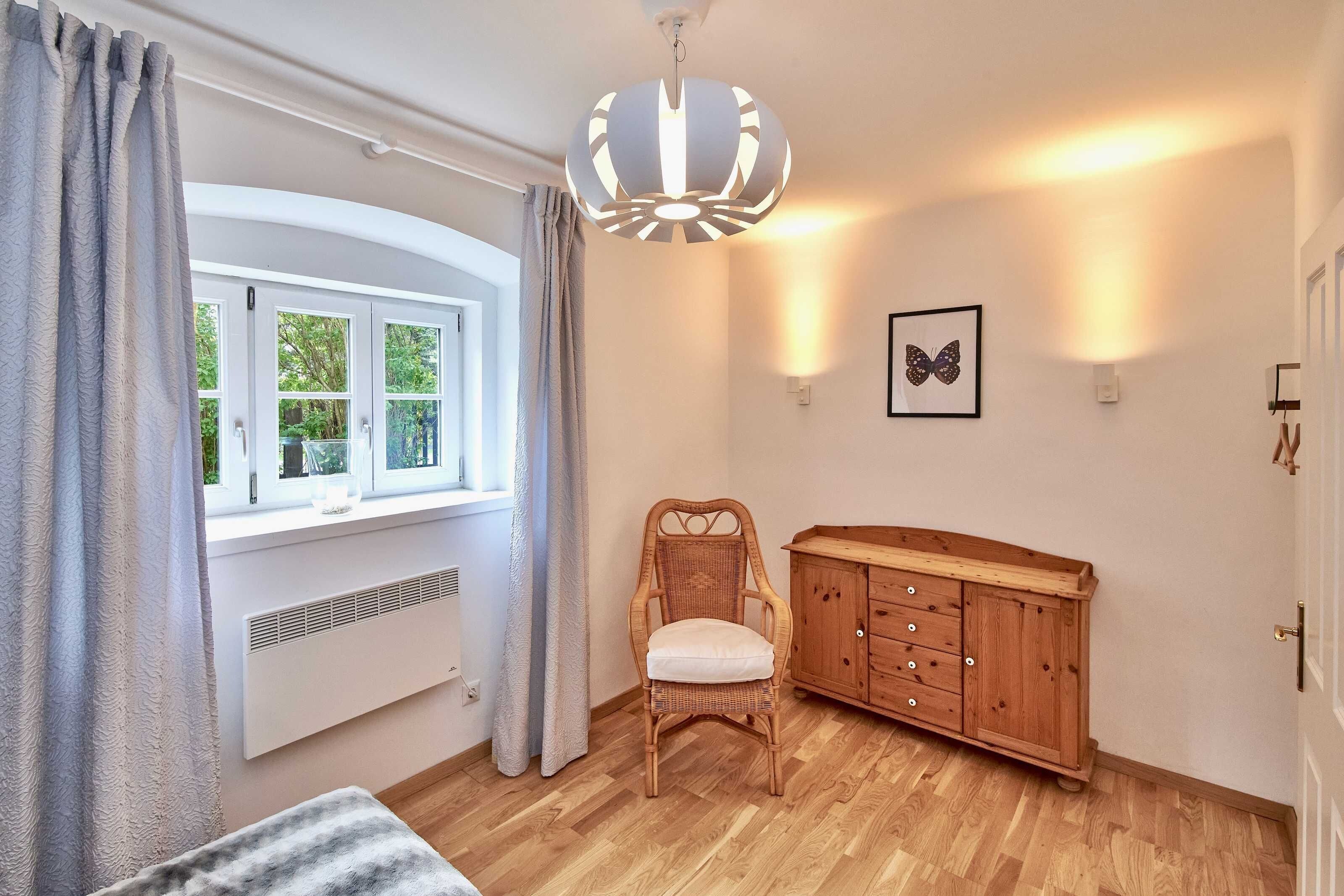 A room with a window, a chair, a wooden cabinet, and a wall-mounted light fixture.