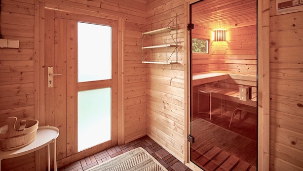 L’intérieur d’un chalet en bois, avec une porte en verre, une table blanche sur laquelle se trouve un bol, et une étagère avec une lampe suspendue.