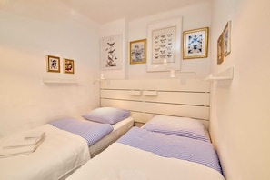 A room with two beds, a white headboard, and wall-mounted shelves with framed artwork. - Landhaus Dodo - Garten Apartment mit Einem SZ - Top 3 - Landhaus Dodo (Payerbach)