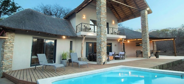 Ein zweistöckiges Haus mit Pool, Steinpfeilern und einem Strohdach.