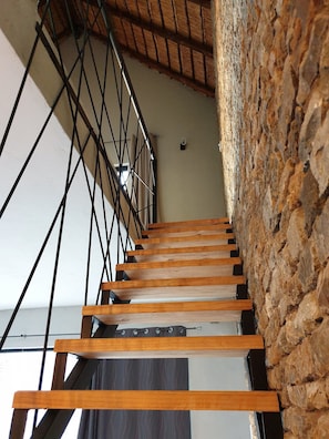 Eine Holztreppe mit Metallgeländern führt zu einem Raum mit einer Steinwand.