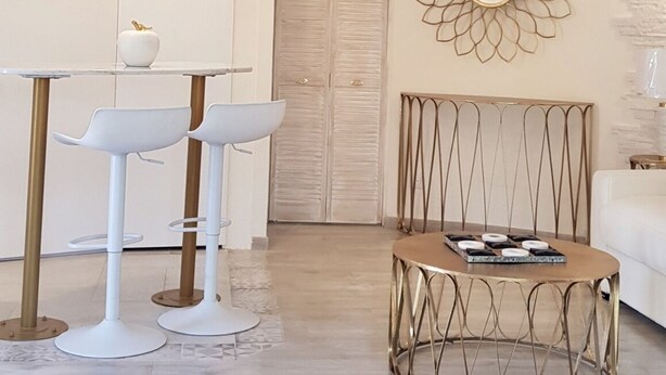 A room with exposed wooden beams, a white wall with a decorative mirror, a round metal table, and two white bar stools. - Studio Indépendant Villa (Mougins)