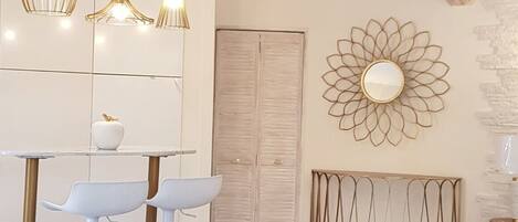 A room with exposed wooden beams, a white wall with a decorative mirror, a round metal table, and two white bar stools.