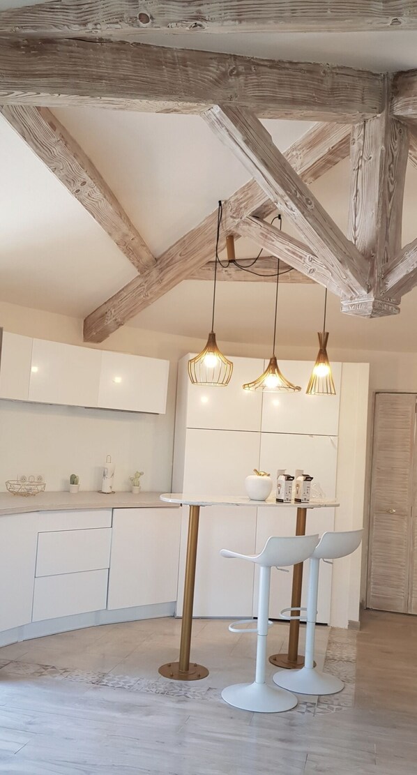 A modern kitchen with white cabinets, a glass-top island, and a wooden ceiling. - Studio Indépendant Villa (Mougins)