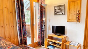 Een kamer met een bed, een televisie op een houten standaard, een klein tafeltje en een deur naar een buitenruimte.