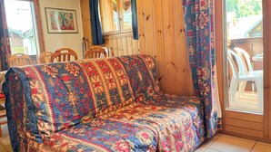 Een gezellige kamer met een houten wand, een gestreept bankstel en een eethoek met stoelen.