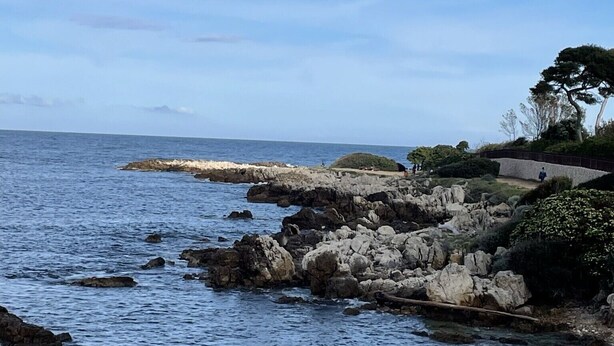 A coastal landscape with rocky shores, a clear sky, and a distant view of the ocean. - Elegant 3 rooms. Tennis pool and greenery. (Antibes)
