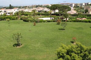 Zona residencial con césped cuidado, varios árboles y una vista distante de una obra en construcción.
