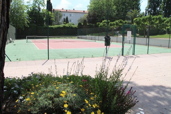 Ein Tennisplatz mit Netz, umgeben von Zäunen und Grünpflanzen.