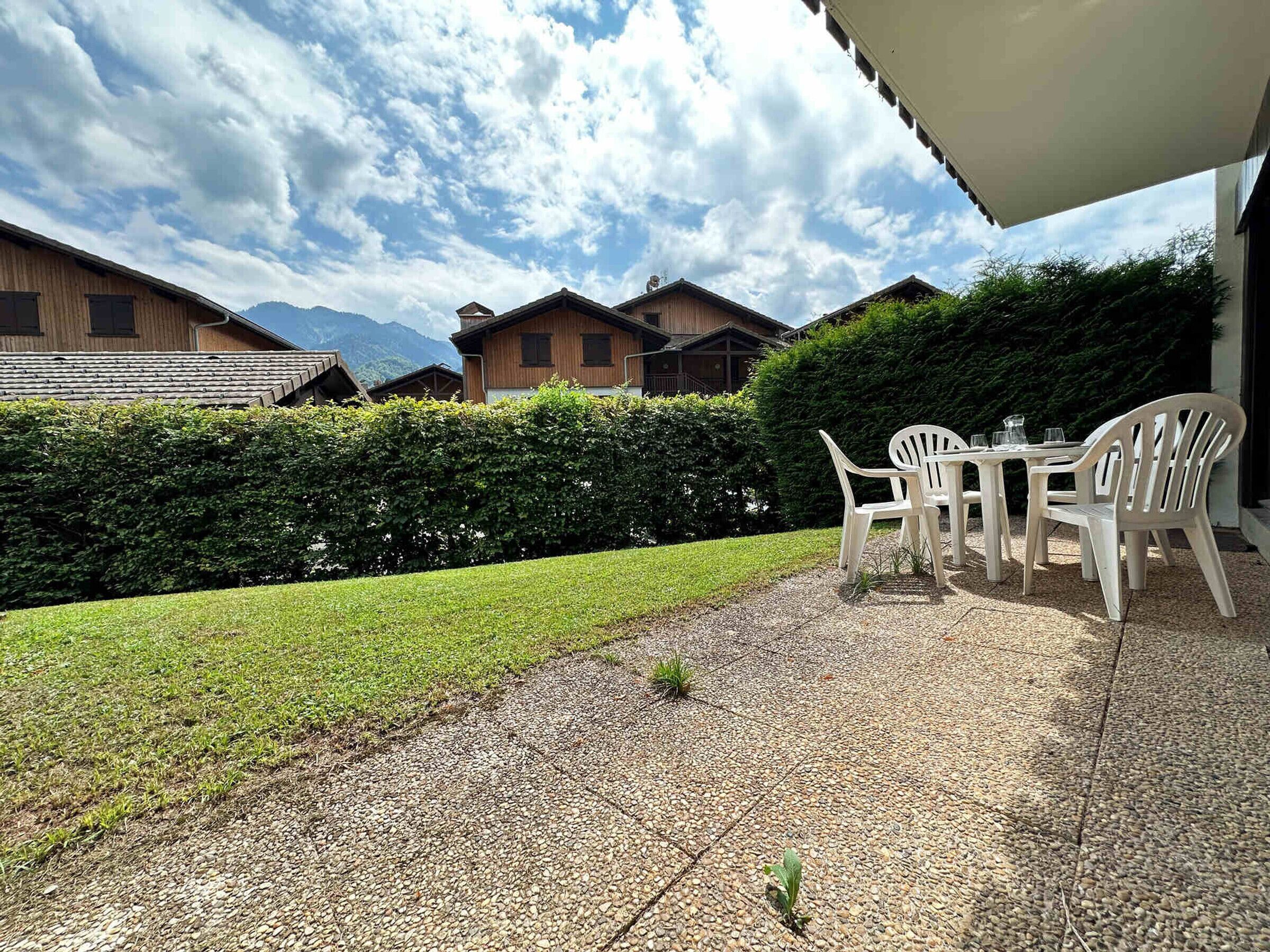 Un espace patio aménagé avec une table et des chaises, un chemin de gravier et une haie soigneusement taillée.