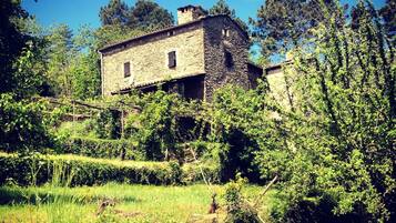 Un bâtiment rustique en pierre, entouré d’une végétation luxuriante et d’arbres.