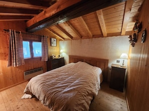 Un dormitorio de cabaña de madera con una cama, mesitas de noche, un aparador y una ventana con cortinas.