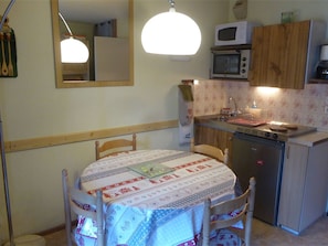A small kitchen with a dining table, chairs, a microwave, a sink, and wooden cabinets.