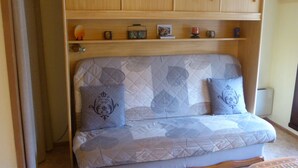 Et værelse med en sovesofa, træskabe og en reol med forskellige ting.