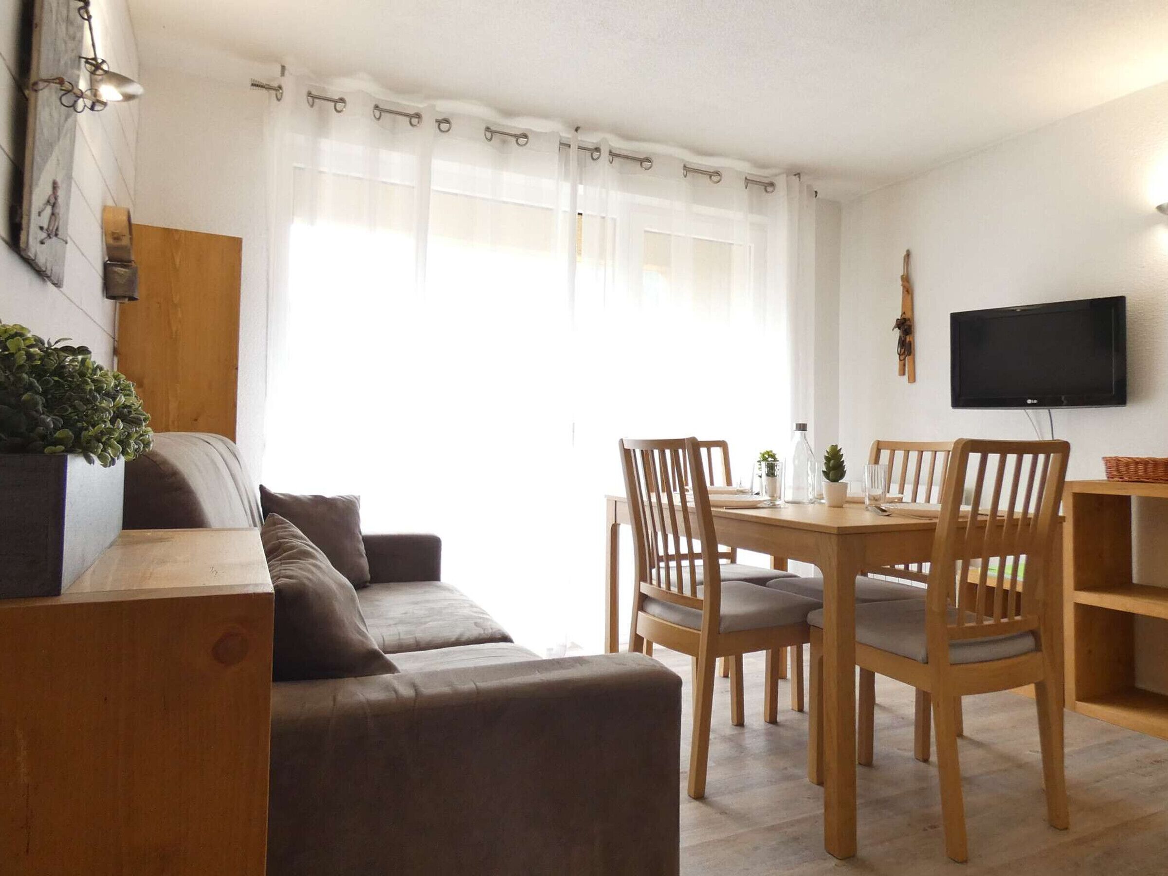 Un salon confortable avec un canapé, une table à manger en bois et des chaises. Un téléviseur est fixé au mur.