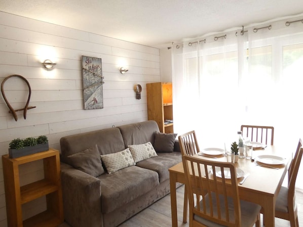 Una sala acogedora con un sofá, mesitas de madera y una mesa de comedor para dos personas.