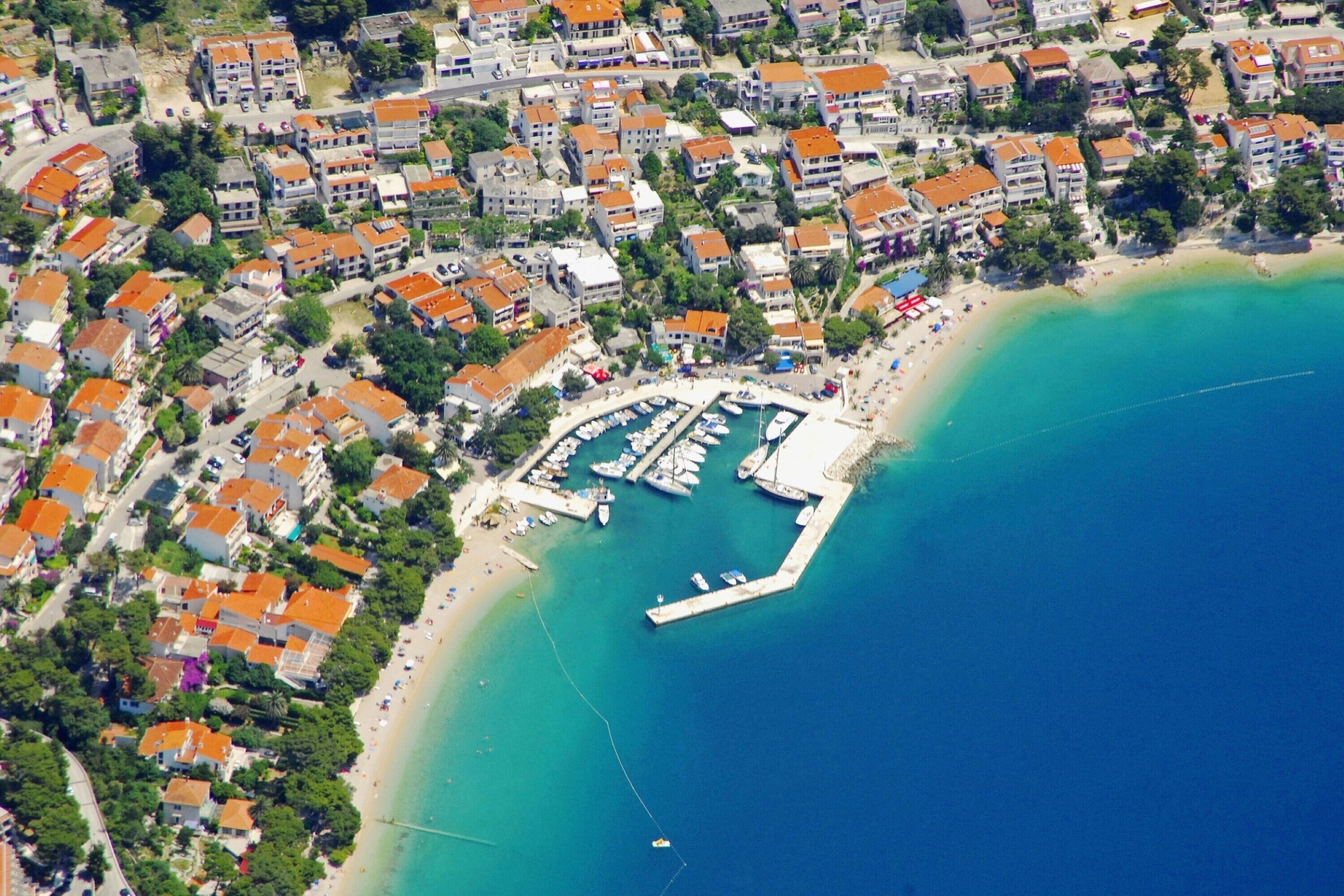 Vue aérienne d’une ville côtière avec des immeubles résidentiels, un port de plaisance et une plage.