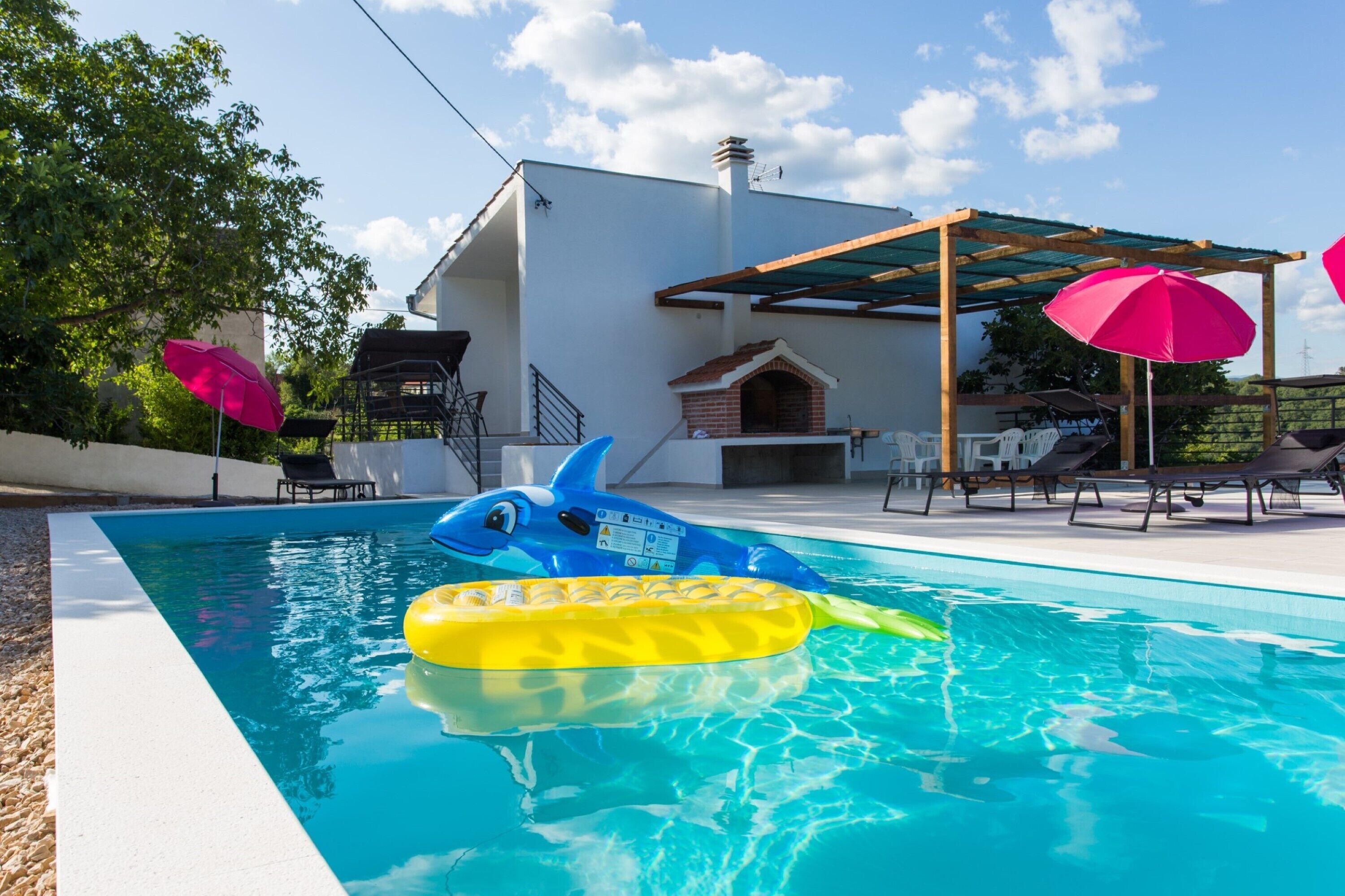 A swimming pool with inflatable toys, a covered patio area, and outdoor seating.