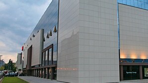 A modern building with a glass facade, a large entrance, and a visible storefront with signage. - Comfortable Apartment With Balcony & Garden View (Split)