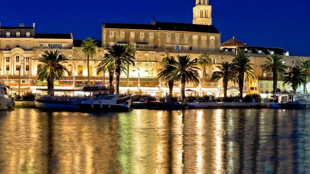 A waterfront hotel with multiple boats docked, a prominent clock tower, and palm trees lining the promenade. - Comfortable Apartment With Balcony & Garden View (Split)