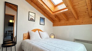 Un dormitorio con techo de madera, una cama con ropa blanca, una silla y un escritorio con lámpara.