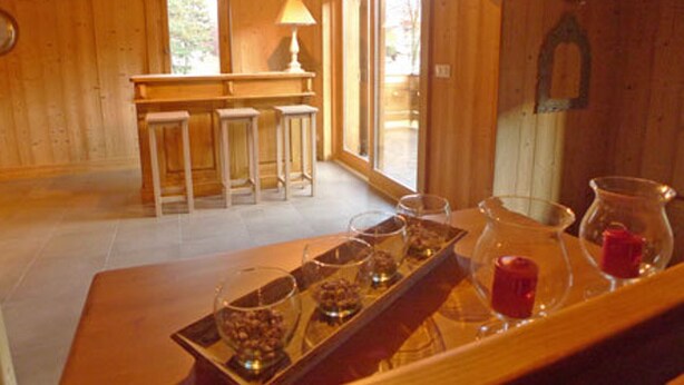 Interior em madeira com área de bar, banquetes e bandeja com copos e uma vela.