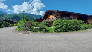 A wooden chalet with a balcony, surrounded by lush greenery and mountains in the background. - Comfortable apartment near center with balcony and parking (Samoëns)