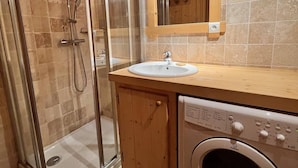 A bathroom with a glass-enclosed shower, a sink with a mirror above it, and a washing machine. - Comfortable apartment near center with balcony and parking (Samoëns)