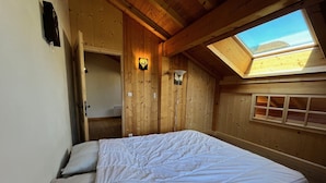 A bedroom with a wooden ceiling, a skylight, a bed with white bedding, and a wooden wardrobe. - Comfortable apartment near center with balcony and parking (Samoëns)