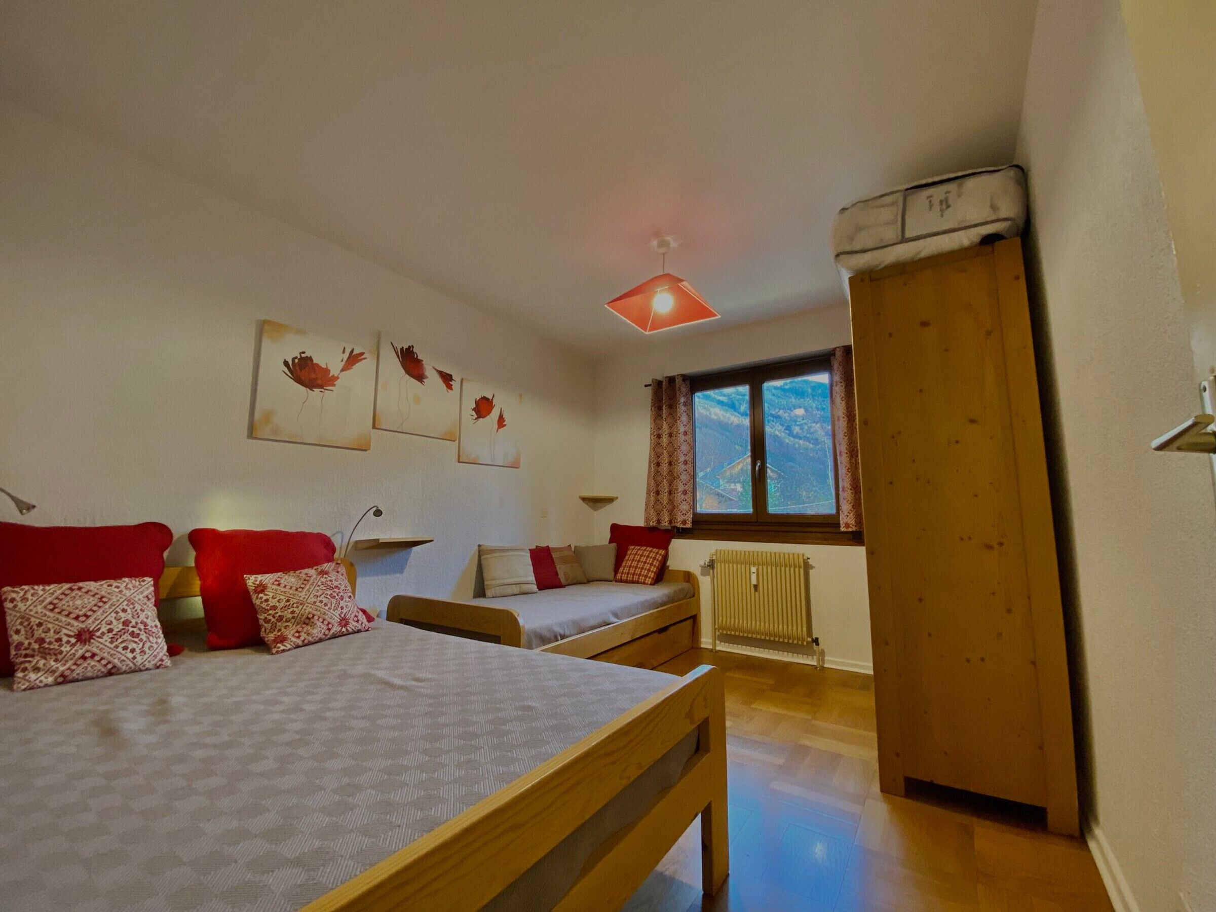 Une chambre avec deux lits, un radiateur, une fenêtre avec des rideaux et des œuvres d’art accrochées au mur.