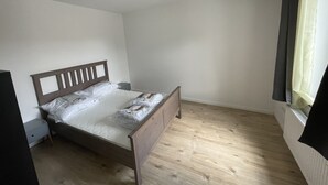 Un dormitorio con una cama de madera, una mesita de noche, una lámpara en el techo y una ventana con cortina.