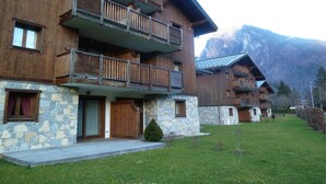 Un edifici de fusta de diversos pisos amb balcons, fonamentació de pedra i un paisatge de muntanyes al fons.