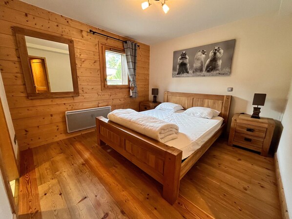 A wooden-paneled bedroom with a bed, a nightstand, a mirror, and a window with curtains.