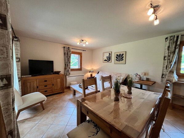 Un coin repas avec une table en bois, des chaises, un téléviseur posé sur un meuble et des œuvres d’art accrochées au mur.