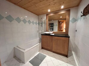A bathroom with a bathtub, a sink, wooden cabinets, and a mirror.