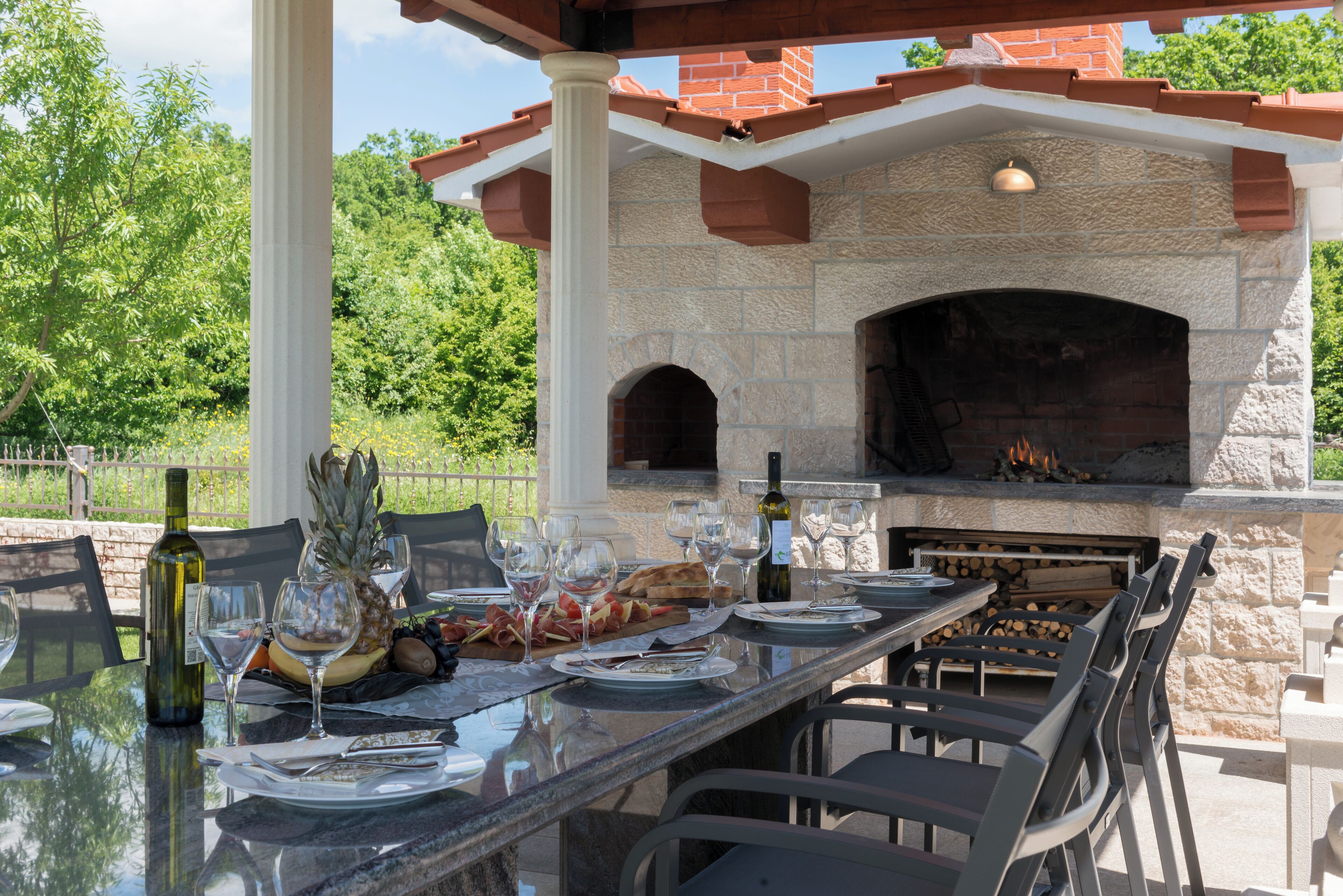 An outdoor dining area with a stone fireplace, a glass table, and chairs.