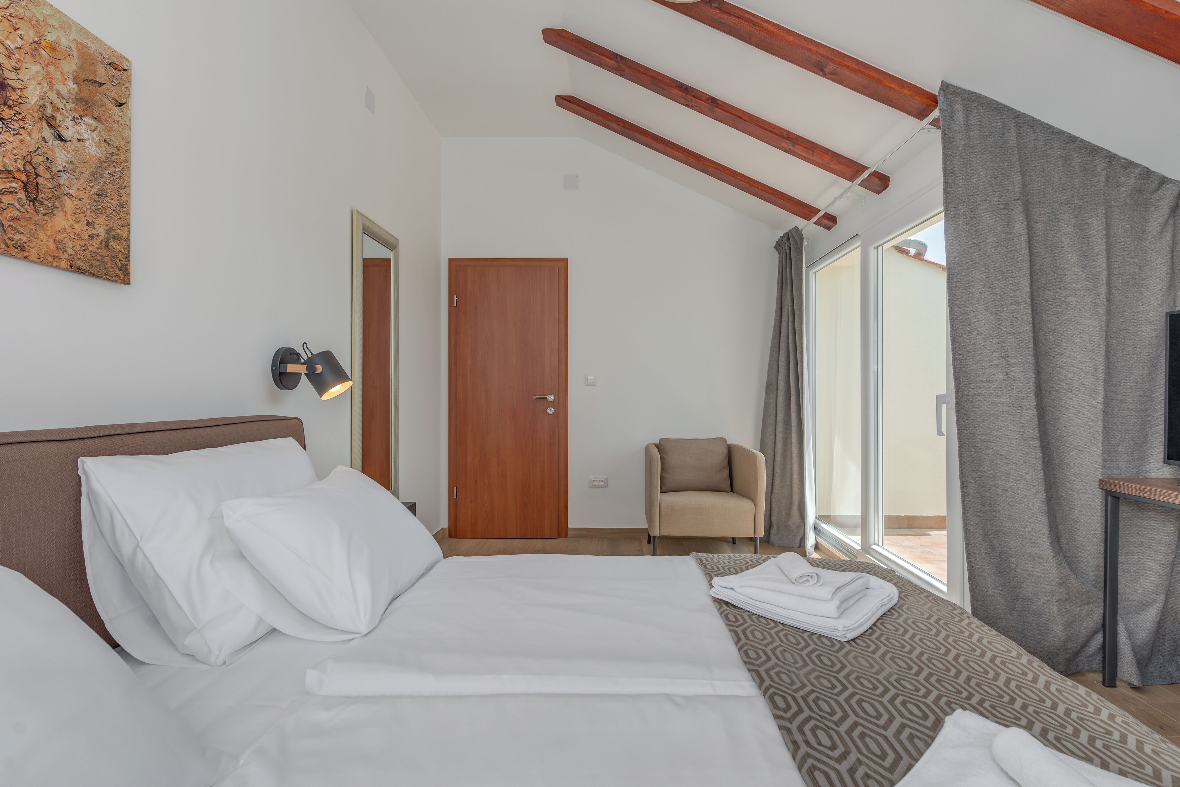 A hotel room with a bed, a chair, a door, and a view of the outdoors.