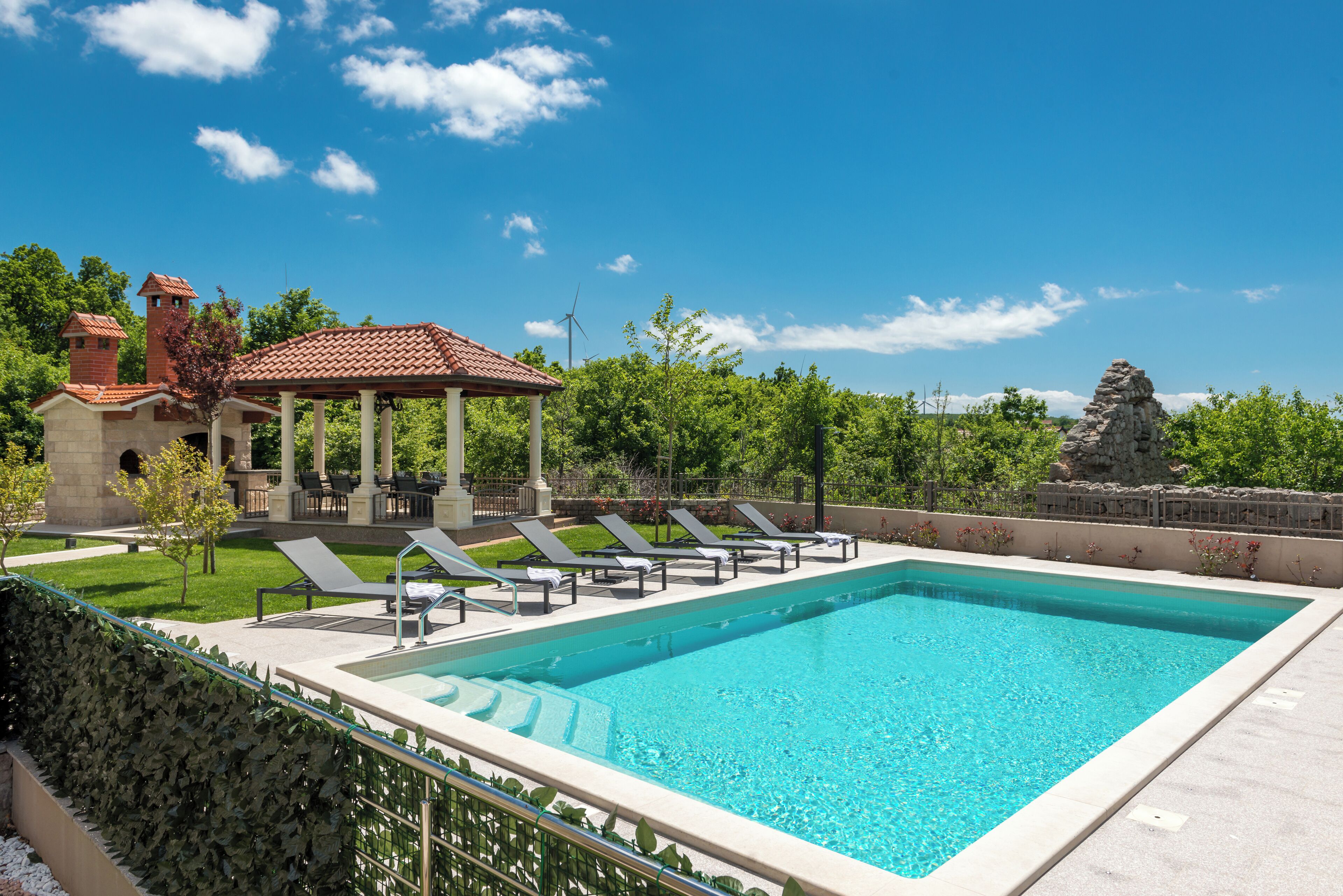 Une piscine rectangulaire, dotée de chaises longues et d’un gazebo.