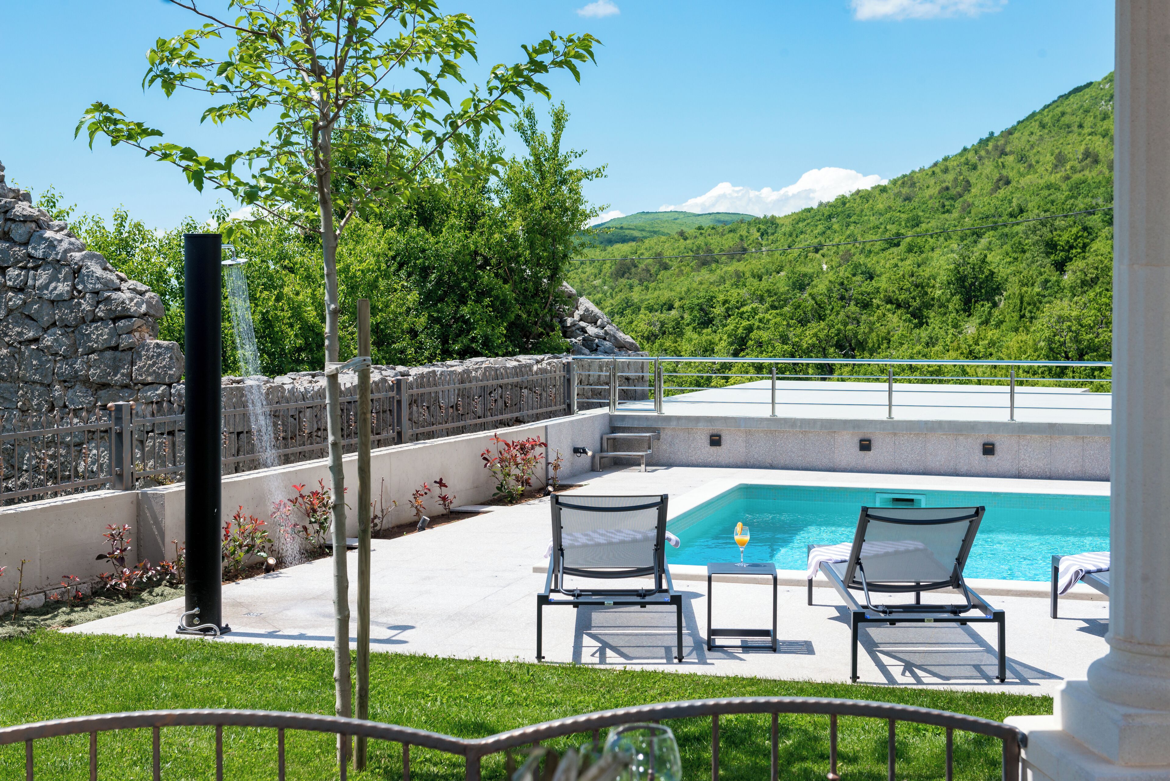 Un espace piscine comprenant deux chaises longues, un mur en pierre et une cascade décorative.