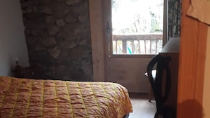 A bedroom with a bed, a wooden ceiling, a stone wall, a window with a view, and a chair. - Chalet in a small village in the Hautes Pyrénées close to walks and hikes (Bareilles)
