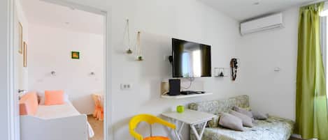 Een compacte woonruimte met een bed, een bank, een kleine tafel, een televisie en een airconditioner.