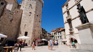 A historic stone tower and buildings in a square with outdoor seating and people walking. - A1 - apt in the Very Heart of Split With sea View (Split)