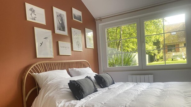 A bedroom with a bed, a window with a view of greenery, and several framed pictures on the wall. - Charming Cottage Near Thoiry Zoo with Private Garden and Modern Amenities (Thoiry)