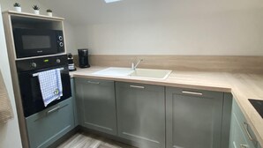 A compact kitchen with a skylight, a microwave, an oven, a coffee maker, and a sink. - Charming Cottage Near Thoiry Zoo with Private Garden and Modern Amenities (Thoiry)