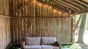 A covered outdoor seating area with a wooden ceiling, a cushioned bench, and a small table. - Charming Cottage Near Thoiry Zoo with Private Garden and Modern Amenities (Thoiry)