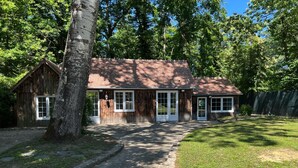 A rustic wooden building with a sloped roof, a front porch, and a pathway leading to the entrance. - Charming Cottage Near Thoiry Zoo with Private Garden and Modern Amenities (Thoiry)